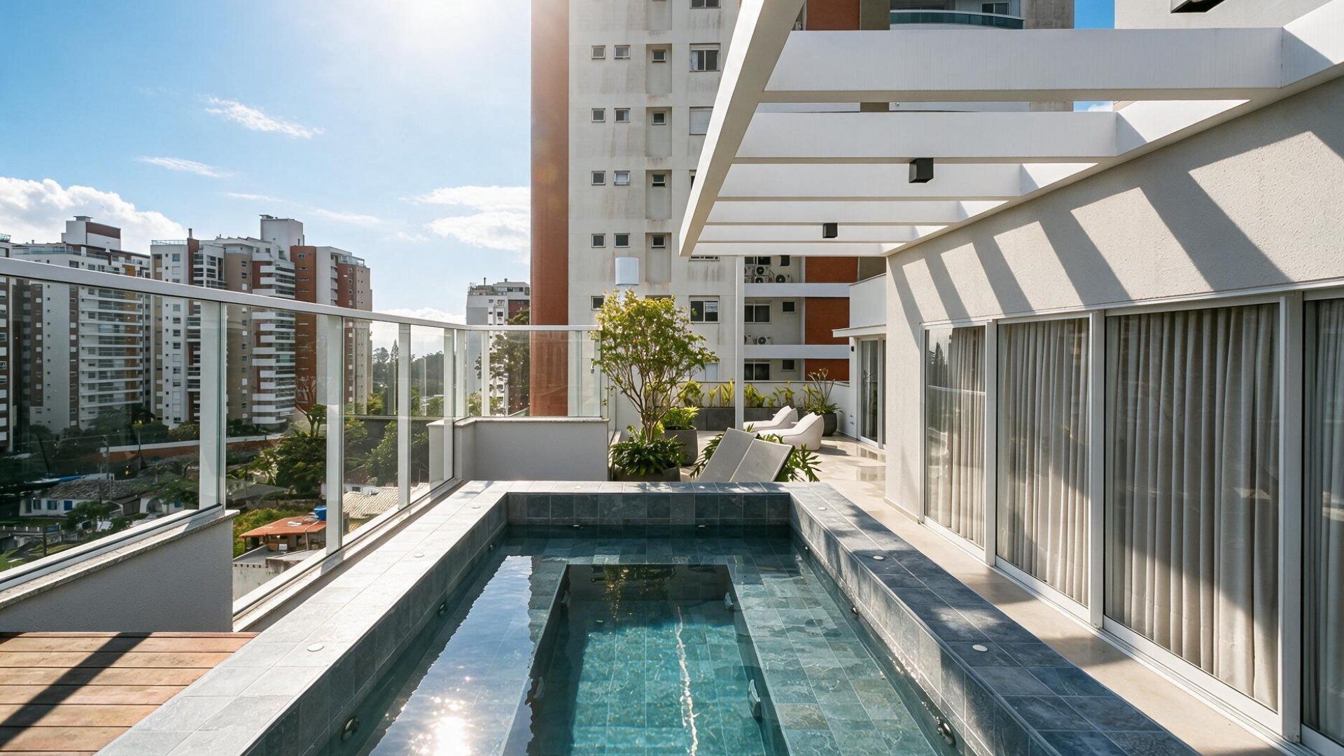 Piscina no terraço com água azul cristalina, rodeada por um edifício moderno com amplas janelas e área de varanda.