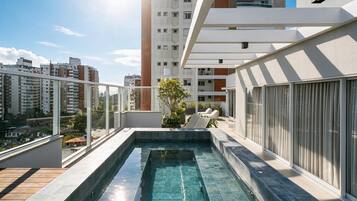 Piscina no terraço com água azul cristalina, rodeada por um edifício moderno com amplas janelas e área de varanda.