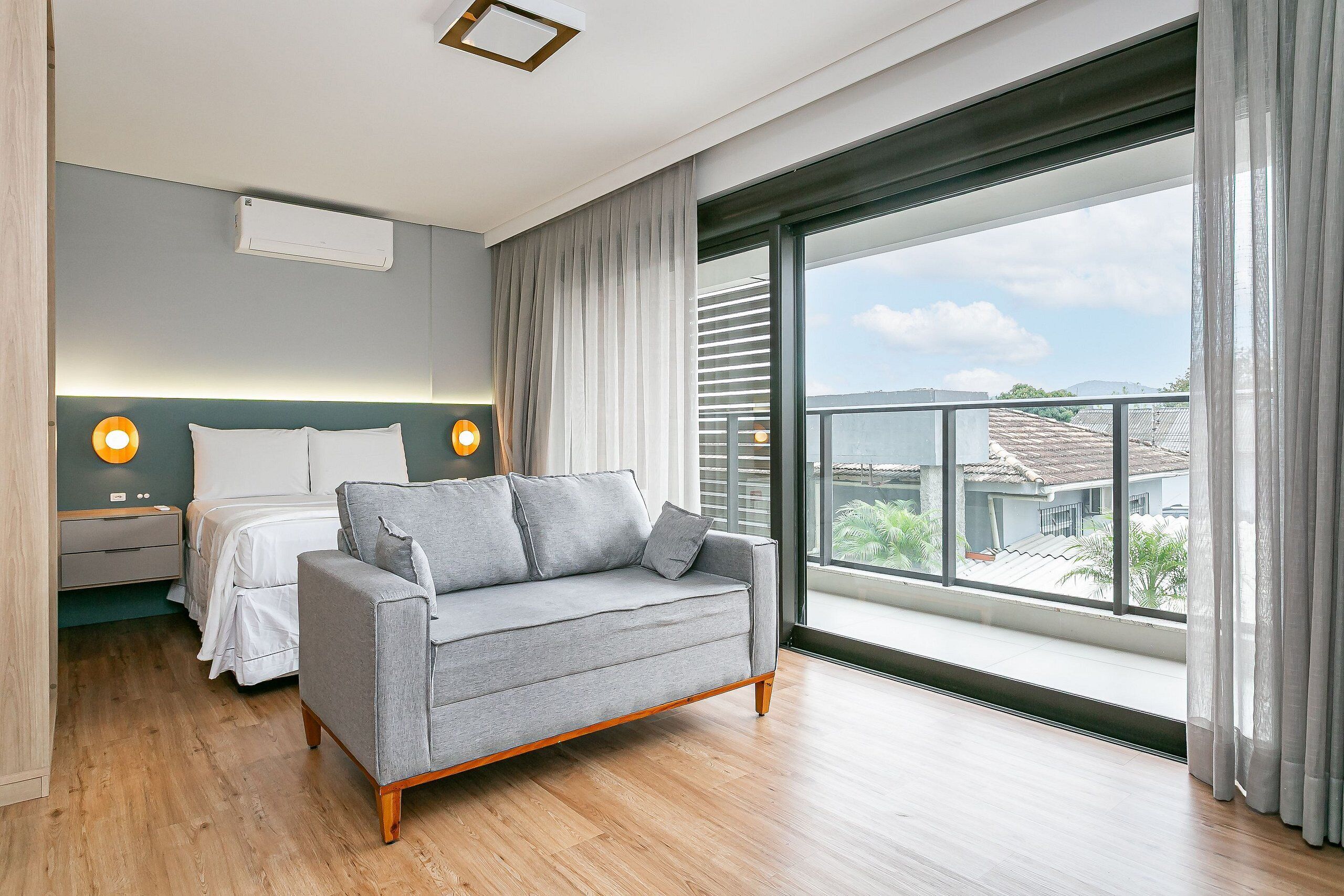 Un dormitorio moderno con un ventanal grande, una cama, un sofá y dos lámparas de noche.