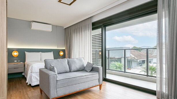 Um quarto moderno com uma janela grande, uma cama, um sofá e duas luminárias de cabeceira.