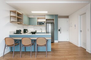 Una cocina moderna con una isla central, electrodomésticos integrados y un comedor con sillas de mimbre.