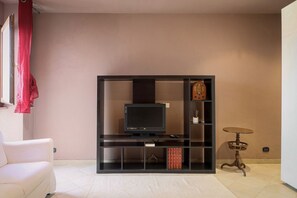 A living room with a television on a black stand, a white sofa, a small table, and a bookshelf. - Hostmate - Bari - Trento (Bari)