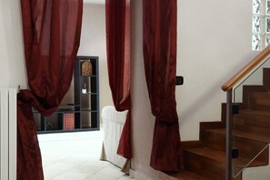 A staircase with a wooden handrail and a glass railing, leading to a landing with a white chair and a red curtain. - Hostmate - Bari - Trento (Bari)