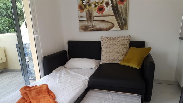 A modern bedroom with a black sofa bed, a white mattress, a yellow pillow, and a large window. - Vacation Apartment 'En Mareverde Resort' with Sea View, Wi-Fi and Air Conditioning (Costa Adeje)