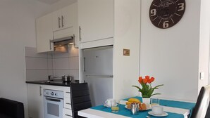 A compact kitchen with modern appliances, a dining area with a table set for breakfast, and a wall clock. - Vacation Apartment 'En Mareverde Resort' with Sea View, Wi-Fi and Air Conditioning (Costa Adeje)