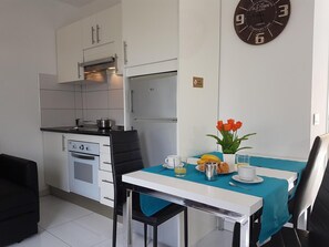 A compact kitchen with modern appliances, a dining area with a table set for breakfast, and a wall clock. - Vacation Apartment 'En Mareverde Resort' with Sea View, Wi-Fi and Air Conditioning (Costa Adeje)