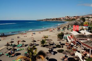 Ein Strand mit Liegestühlen und Sonnenschirmen, ein McDonald's Restaurant und im Hintergrund Meer und Gebäude.