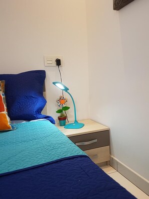 Ein Schlafzimmer mit einem Bett, einem Nachttisch, einer Lampe und einem Blumentopf.