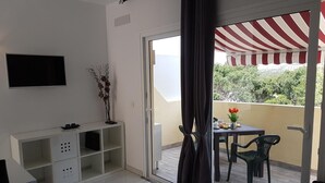 A modern living room with a flat-screen TV, a white console table, and a balcony with a striped awning. - Vacation Apartment 'En Mareverde Resort' with Sea View, Wi-Fi and Air Conditioning (Costa Adeje)