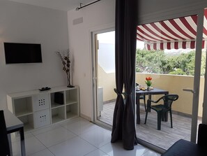 A modern living room with a flat-screen TV, a white console table, and a balcony with a striped awning. - Vacation Apartment 'En Mareverde Resort' with Sea View, Wi-Fi and Air Conditioning (Costa Adeje)