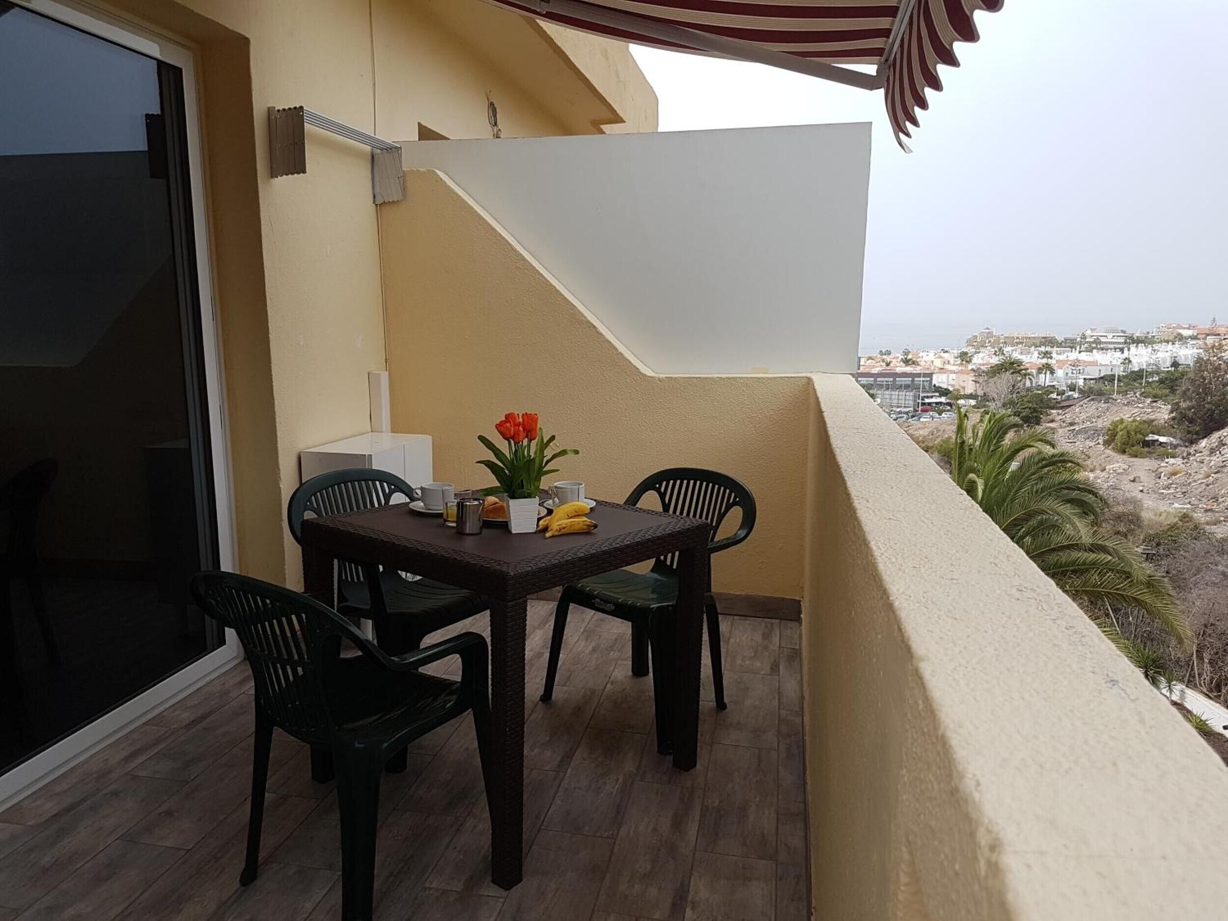 A balcony with a table and chairs, a small plant, and a view of a cityscape.