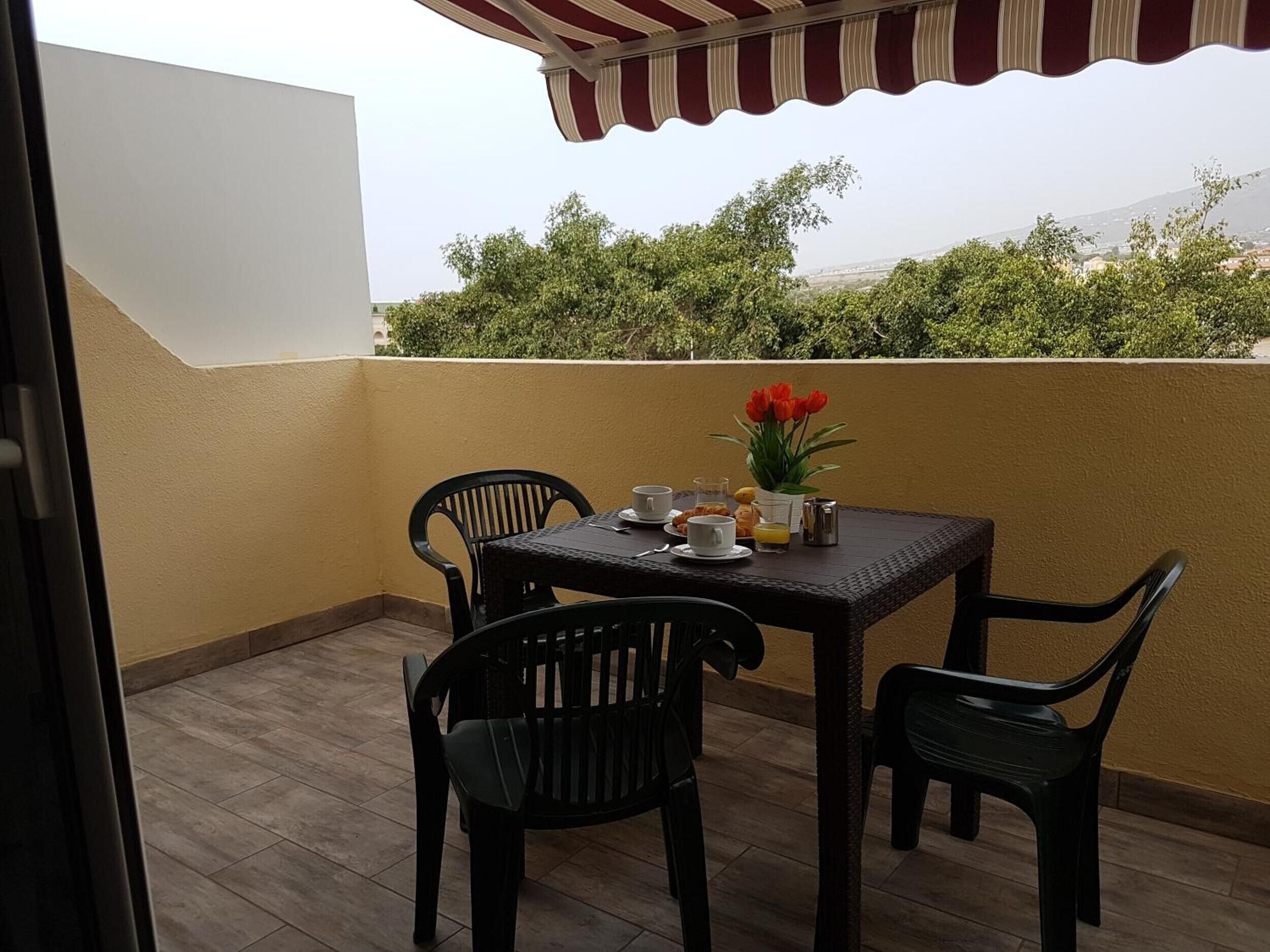 Ein Balkon mit Tisch und Stühlen für zwei Personen, einer kleinen Pflanze und Blick auf Grünflächen und Gebäude.