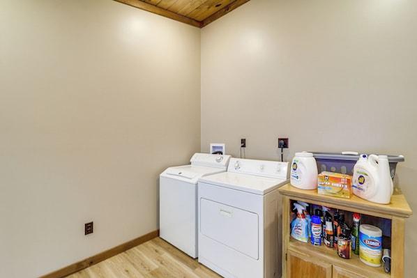 A laundry room with two white washing machines, a shelf with cleaning supplies, and a wooden floor.