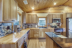 A modern kitchen with wooden cabinets, a granite countertop, a microwave, a stove, and a refrigerator.