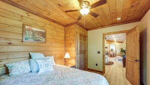 A wooden-paneled bedroom with a bed, a ceiling fan, and a painting on the wall.