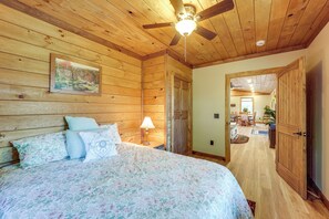 A wooden-paneled bedroom with a bed, a ceiling fan, and a painting on the wall.