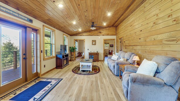 A spacious living room with wooden walls and ceiling, a large sofa, a coffee table, and a television.