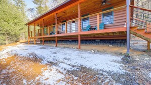 A wooden cabin with a covered porch, multiple windows, and a staircase leading to an upper level.