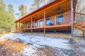 A wooden cabin with a covered porch, multiple windows, and a staircase leading to an upper level.