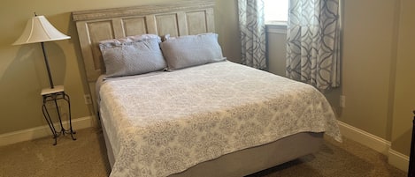 A bedroom with a bed, a nightstand, a lamp, and a window with patterned curtains.
