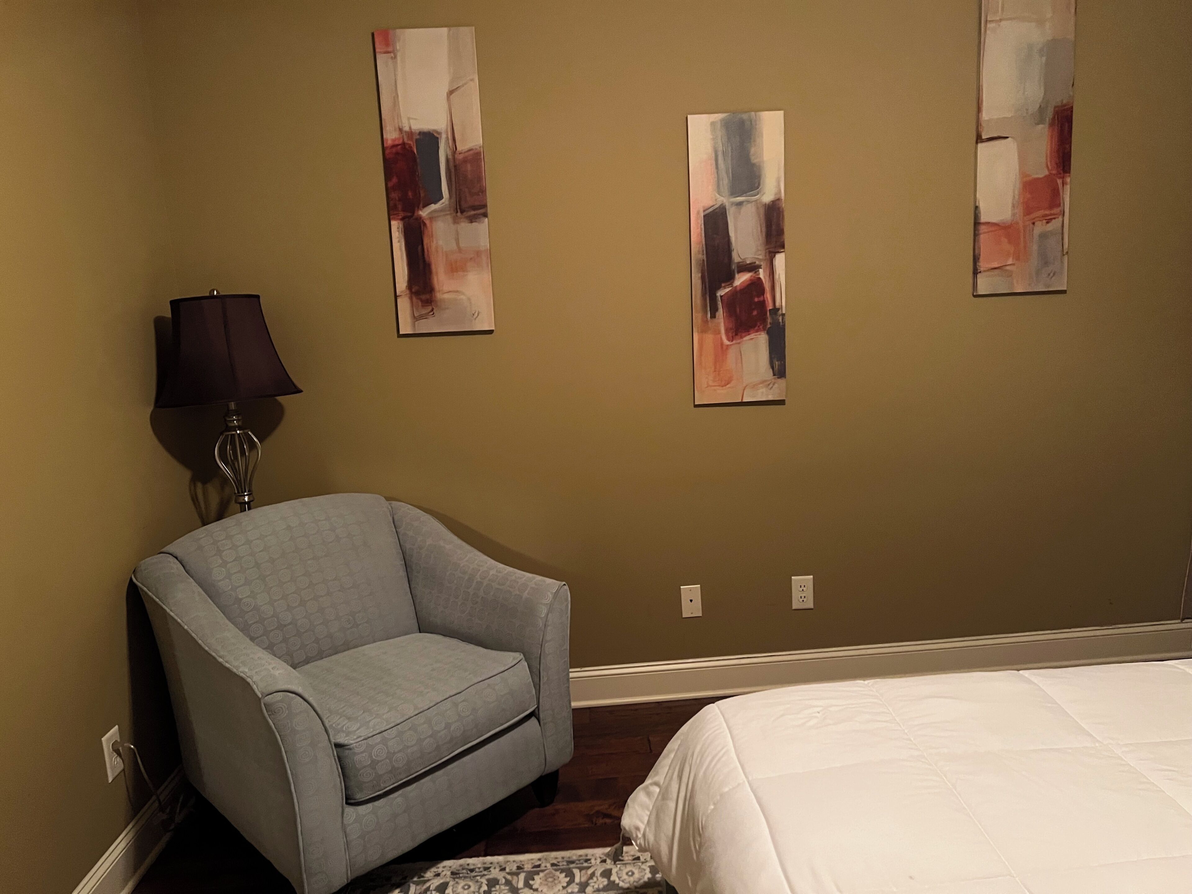 Un dormitorio con una cama, una silla y arte abstracto en la pared.