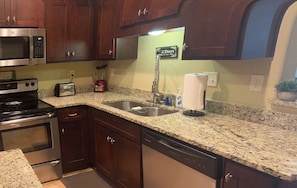 Una cocina con armarios de madera oscura, un microondas de acero inoxidable, un tostador, una cafetera y un lavavajillas.