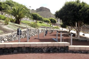 A pathway with exercise equipment, a stone wall, and trees. - 'El Galeón' Bright Apartment with Partial Sea View, Pool, and Wi-Fi (Adeje)