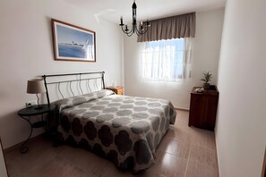 A bedroom with a bed, bedside table, lamp, nightstand, window with curtains, and a painting on the wall. - 'El Galeón' Bright Apartment with Partial Sea View, Pool, and Wi-Fi (Adeje)