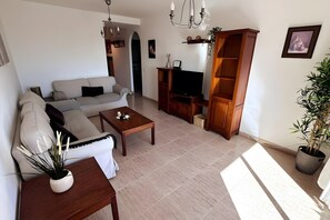 A living room with a sofa, coffee table, TV stand, and a bookshelf. - 'El Galeón' Bright Apartment with Partial Sea View, Pool, and Wi-Fi (Adeje)