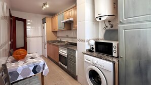 A compact kitchen with a washing machine, microwave, and a table with a patterned tablecloth. - 'El Galeón' Bright Apartment with Partial Sea View, Pool, and Wi-Fi (Adeje)