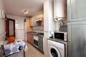 A compact kitchen with a washing machine, microwave, and a table with a patterned tablecloth. - 'El Galeón' Bright Apartment with Partial Sea View, Pool, and Wi-Fi (Adeje)