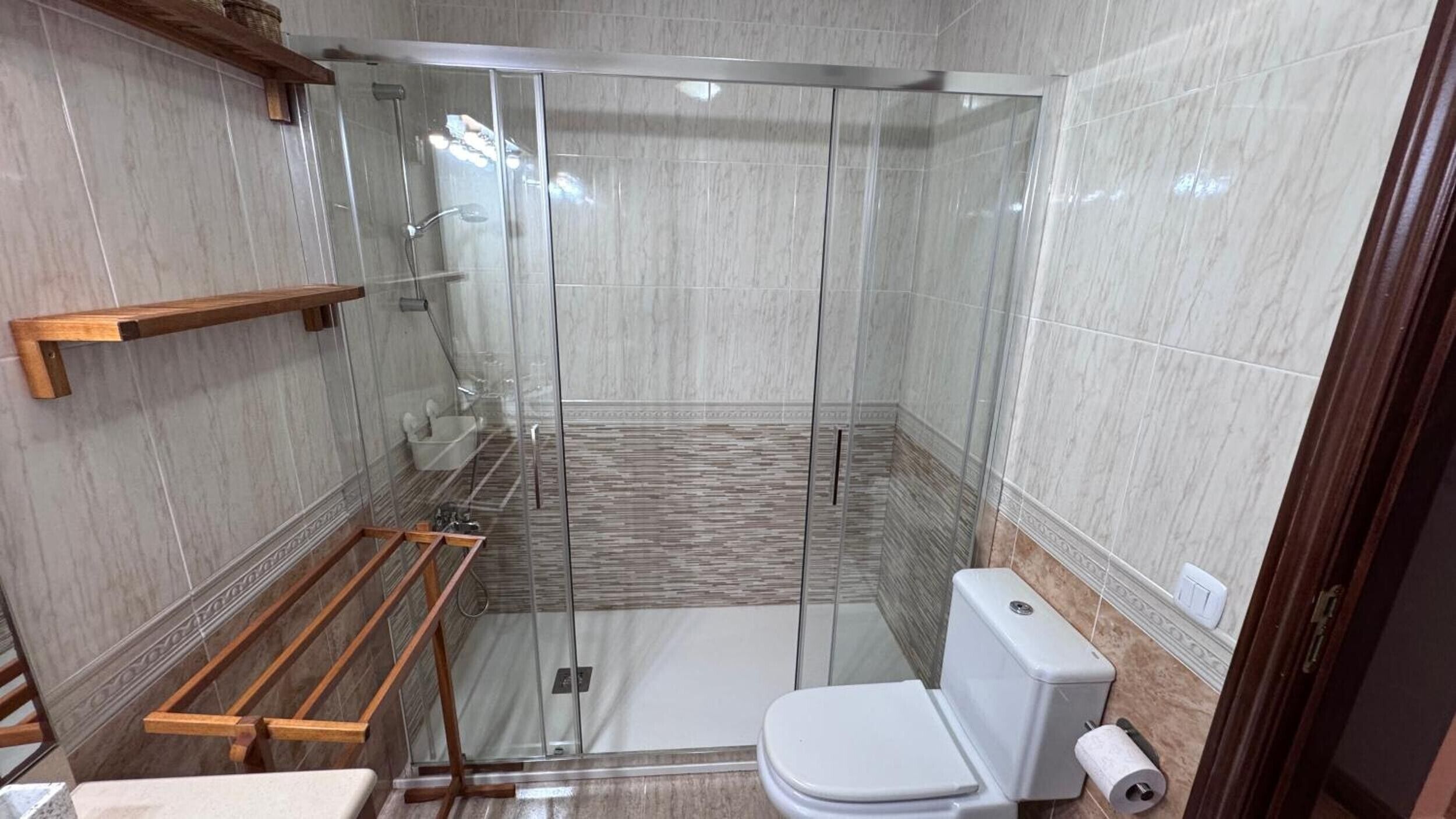 A modern bathroom with a glass shower enclosure, a toilet, and a wooden shelf.