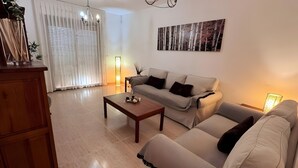 A living room with a sofa, a coffee table, a chandelier, and a painting on the wall. - 'El Galeón' Bright Apartment with Partial Sea View, Pool, and Wi-Fi (Adeje)