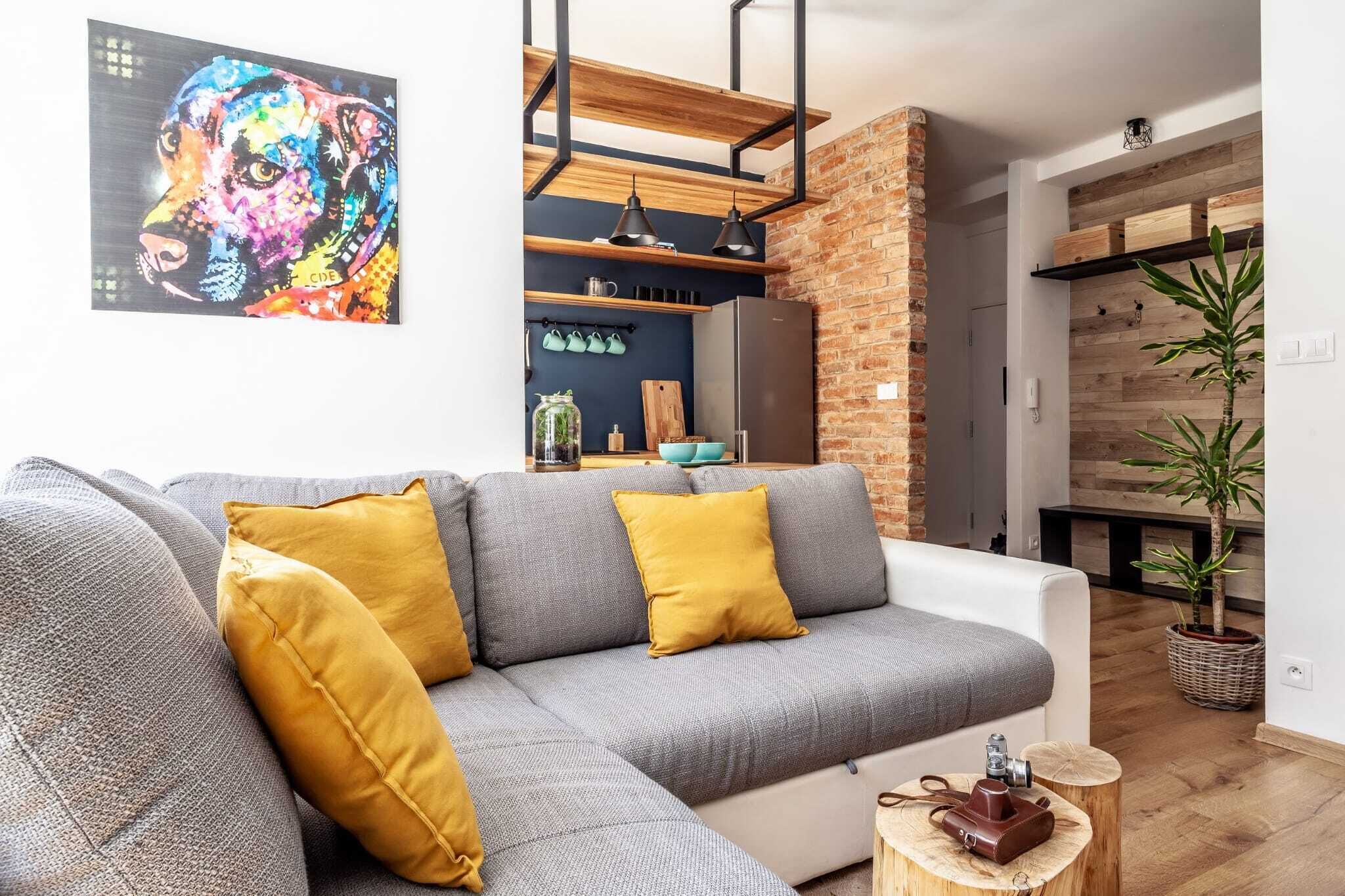 A modern living room with a grey sectional sofa, yellow cushions, a wooden coffee table, and a colorful abstract painting on the wall.