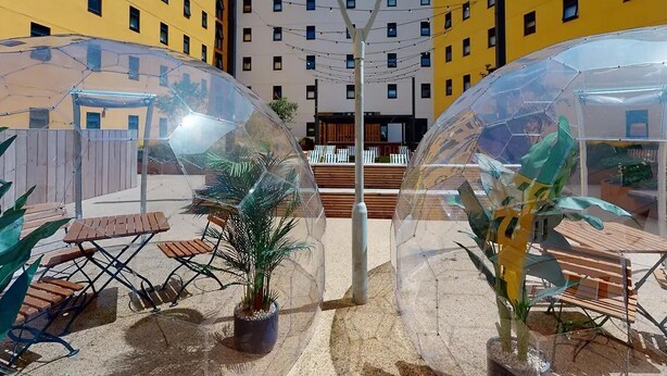 A courtyard with transparent dome structures, seating areas, and a central light pole. - Student Only Seren (Swansea)