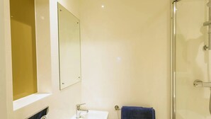 A bathroom with a glass shower enclosure, a white sink, and a mirror. - Student Only Seren (Swansea)