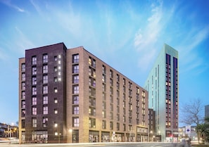 Ein mehrstöckiges Hotel mit Backsteinfassade und ein modernes Glasgebäude direkt daneben.