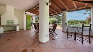 Eine Außenpatio mit einer Holzpergola, Fliesenböden und einem Essbereich mit Stühlen und einem Tisch.