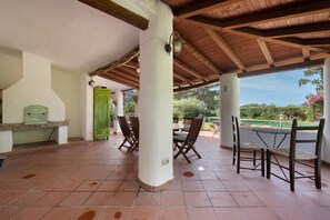 Eine Außenpatio mit einer Holzpergola, Fliesenböden und einem Essbereich mit Stühlen und einem Tisch.