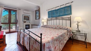 Ein Schlafzimmer mit einem Bett, zwei Nachttischlampen, einem Fenster mit Vorhängen, einer Wand-Klimaanlage und Blick ins Freie.