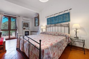 Ein Schlafzimmer mit einem Bett, zwei Nachttischlampen, einem Fenster mit Vorhängen, einer Wand-Klimaanlage und Blick ins Freie.
