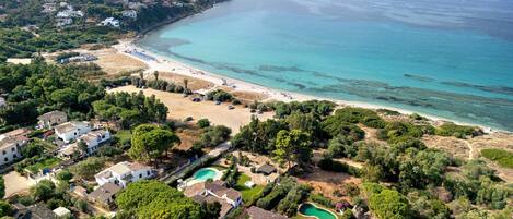 A coastal property with multiple buildings, a beach, and a clear view of the sea.