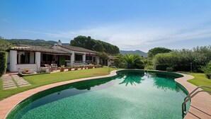 Ein Schwimmbecken mit einer gefliesten Kante, umgeben von einer Terrasse mit Gartenmöbeln.