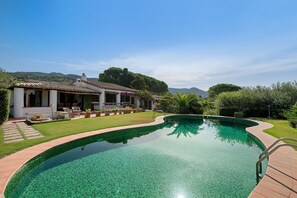 Ein Schwimmbecken mit einer gefliesten Kante, umgeben von einer Terrasse mit Gartenmöbeln.