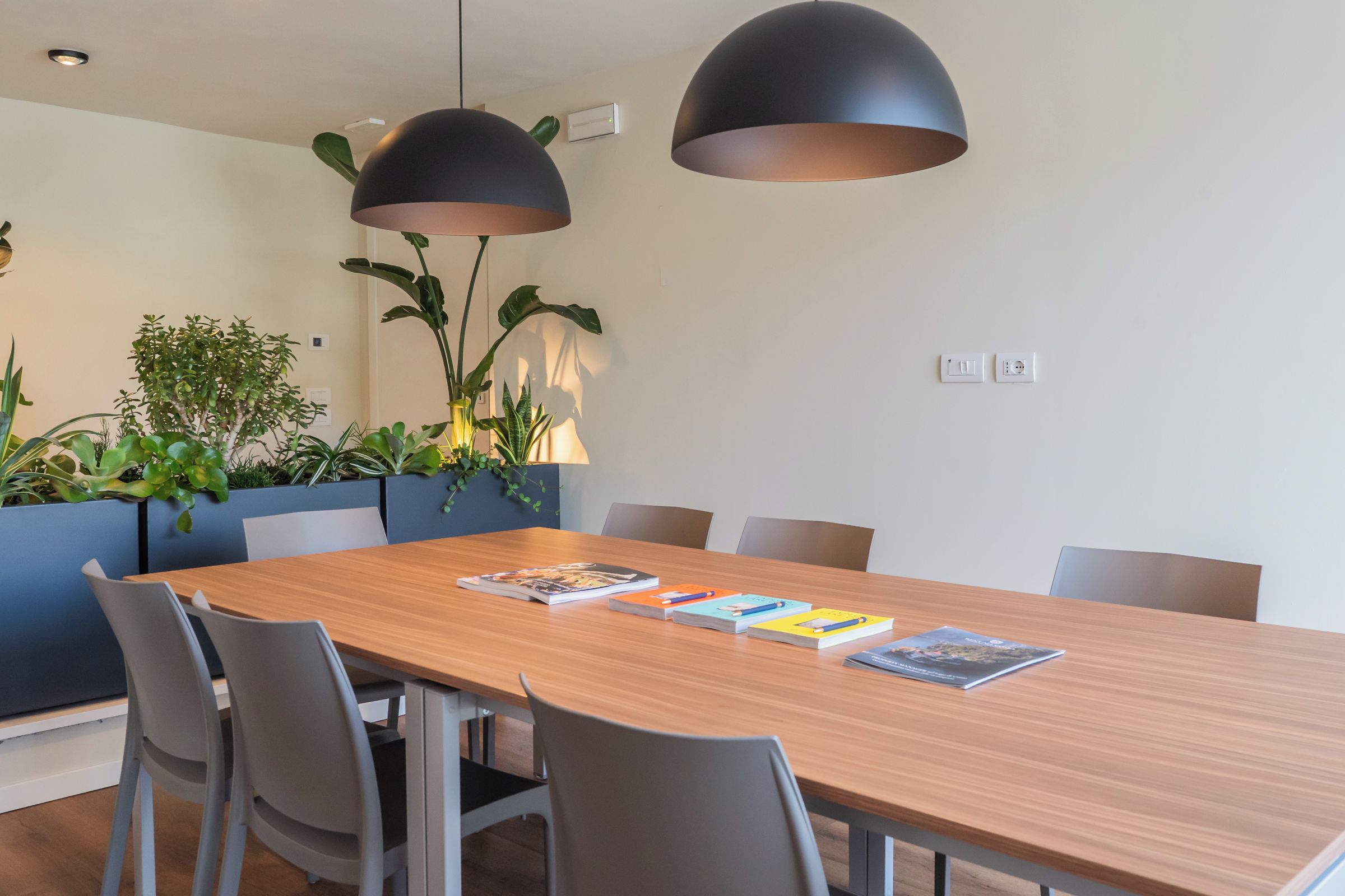 Uma sala de jantar moderna com uma mesa de madeira, cadeiras cinzas e duas luminárias pendentes.
