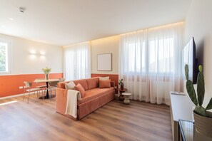 A modern living room with a sofa, a dining table with chairs, a TV, and a cactus plant. - Circle - Pigra - Two Bedroom Apartment, Sleeps 6 (Como)