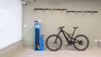 Eine Fahrradreparaturstation mit einem Fahrrad, einer Luftpumpe und einem an der Wand befestigten Fahrradständer, alles in einem Raum mit Fliesenboden.