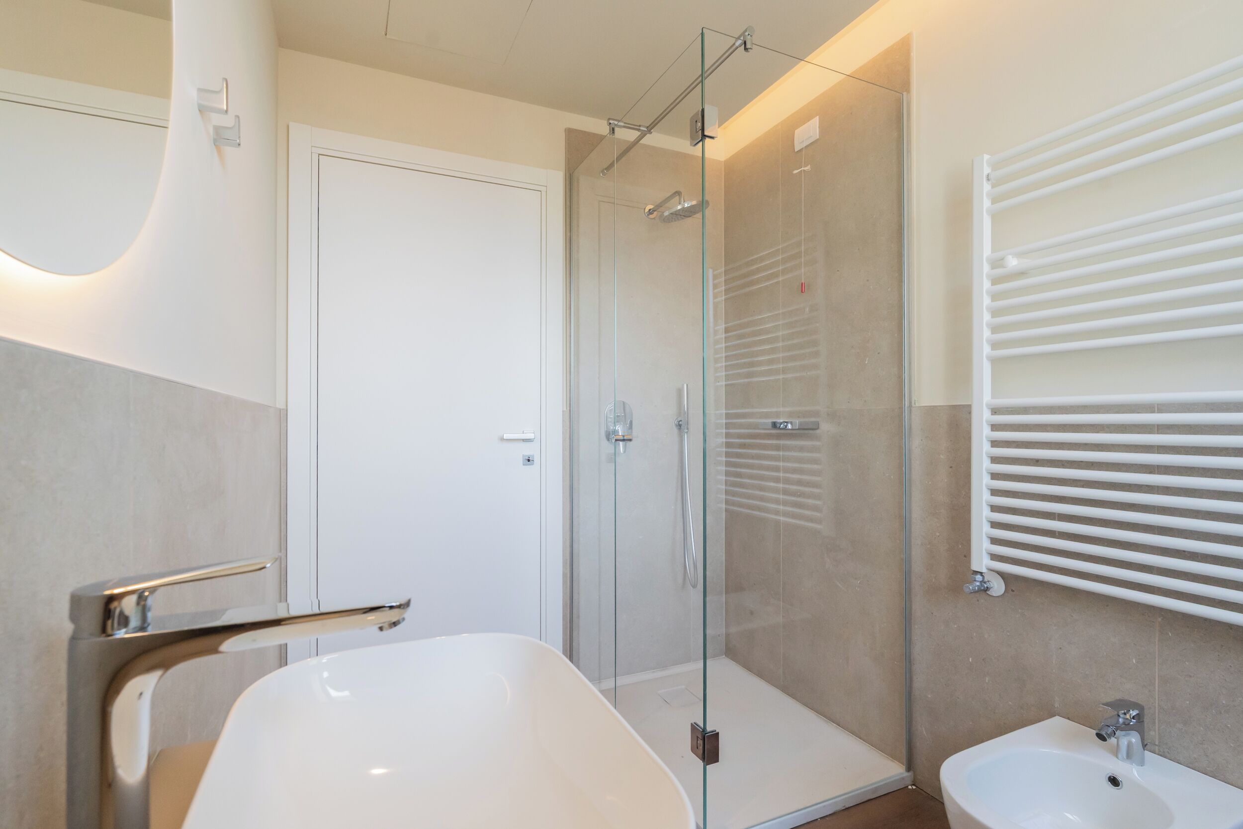 Ein modernes Badezimmer mit einer begehbaren Glasdusche, einer freistehenden Badewanne und einem Waschbecken auf Säule.