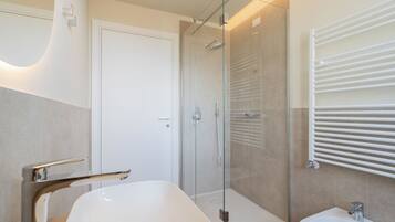 Ein modernes Badezimmer mit einer begehbaren Glasdusche, einer freistehenden Badewanne und einem Waschbecken auf Säule.