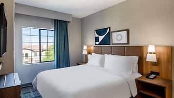 Een hotelkamer met een groot bed, een bureau, een stoel, een raam met gordijnen en een aan de muur bevestigd telefoontoestel.